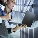 two colleagues discussing work while holding a laptop